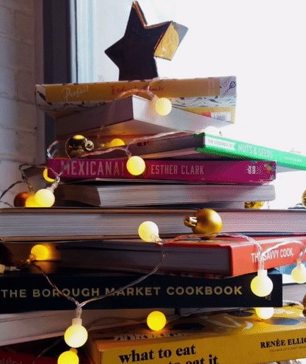Kirjoja koottu joulukuusen muotoon pöydälle, koristeena valot ja tähti.